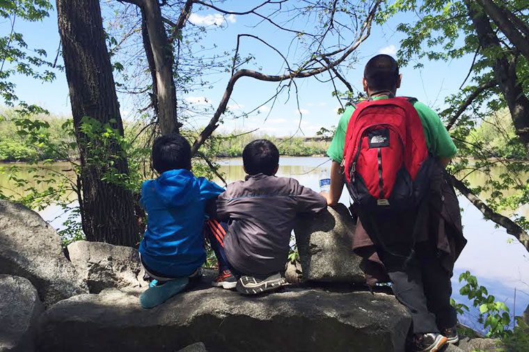 Three kids sitting on a rock near the water.